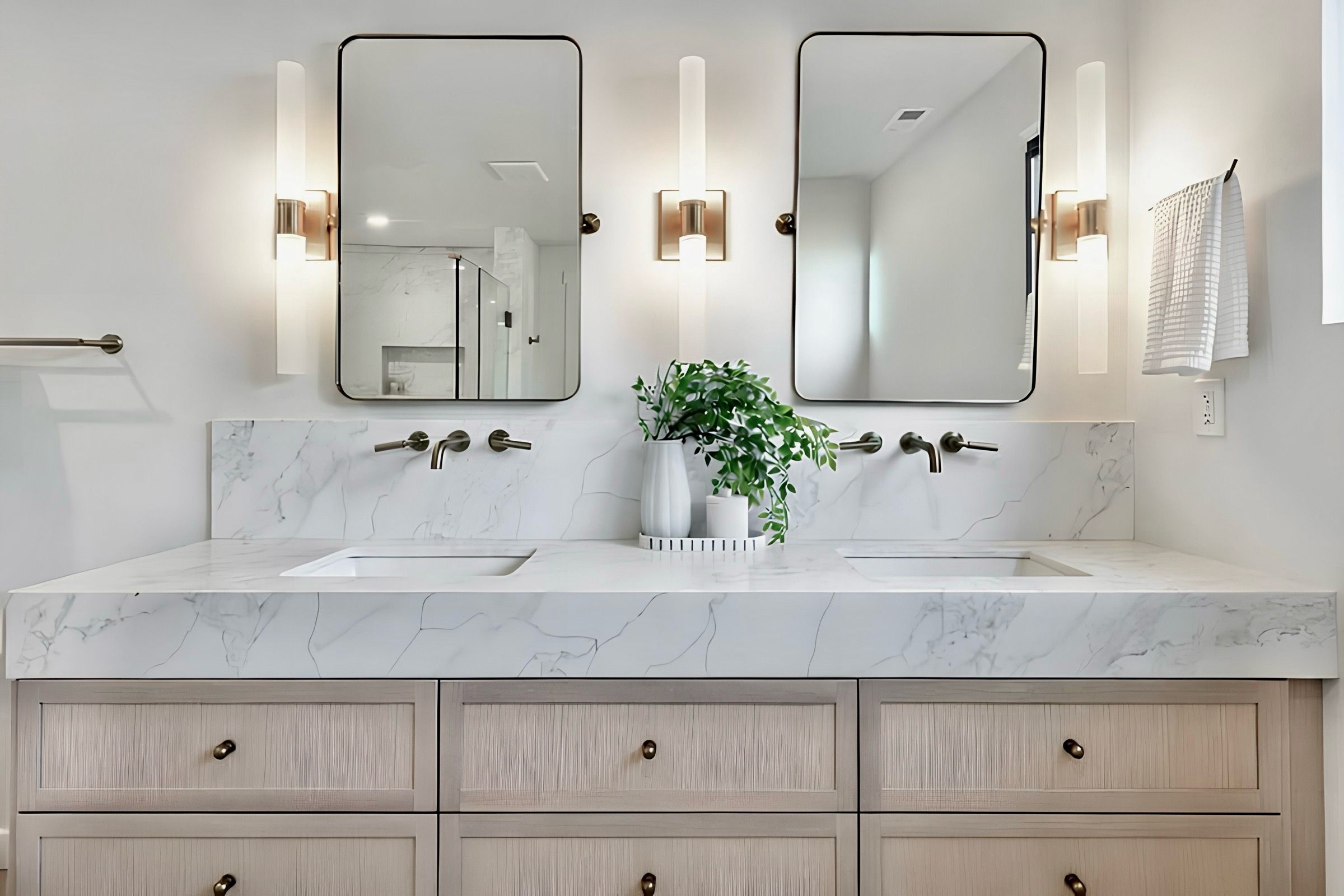 A double-vanity bathroom with marble counters, wood cabinetry and brass fixtures