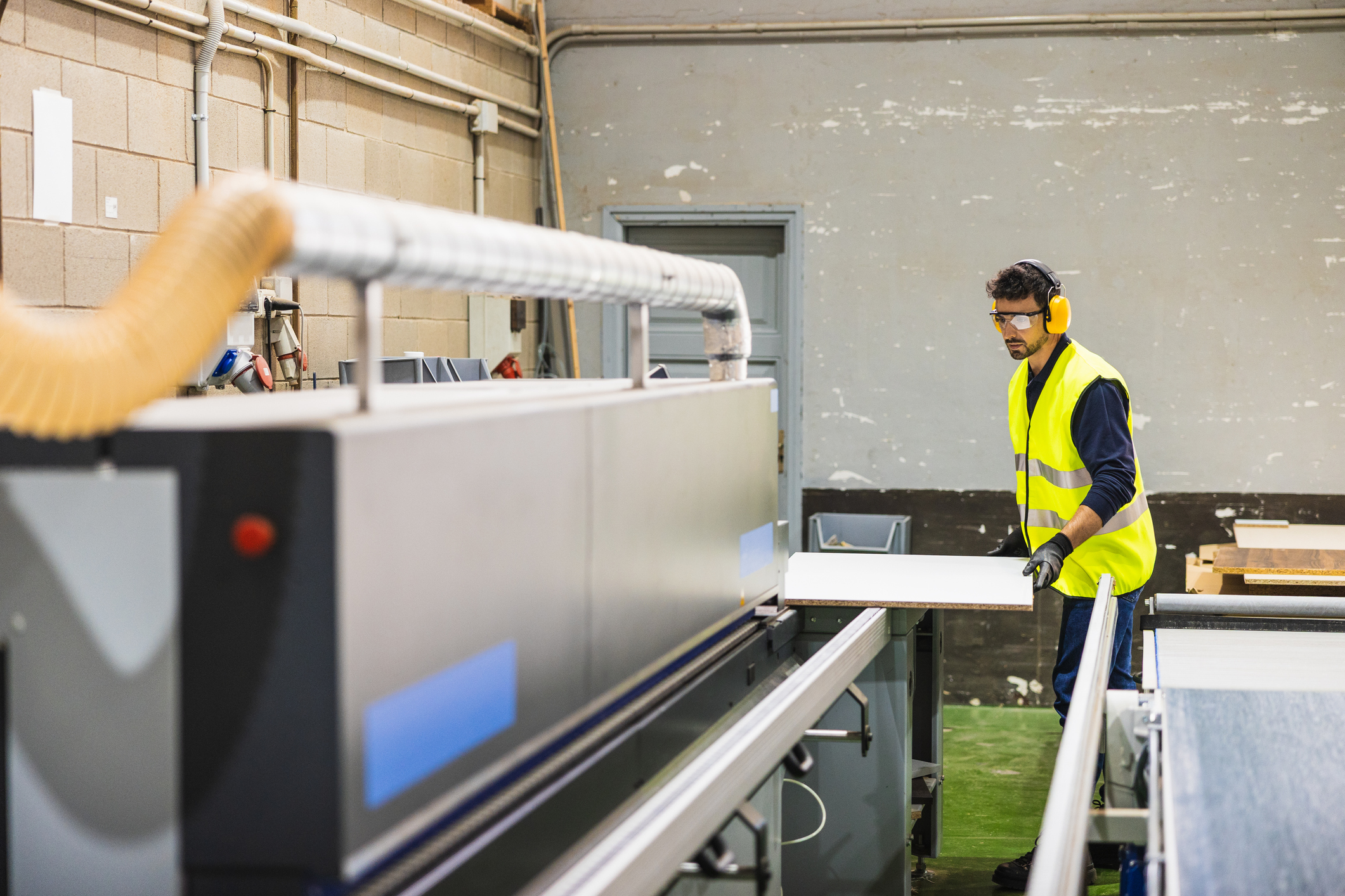 A worker in safety gear feeding a panel through a machine on a cabinet factory line