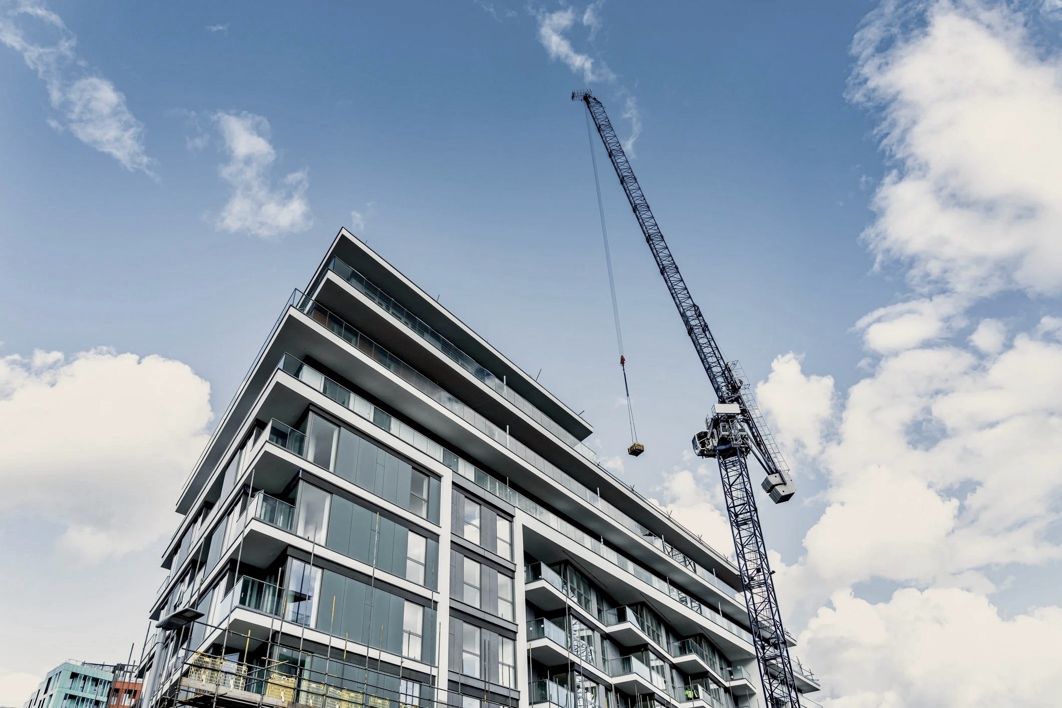 A modern residential building under construction with a tower crane against a blue sky