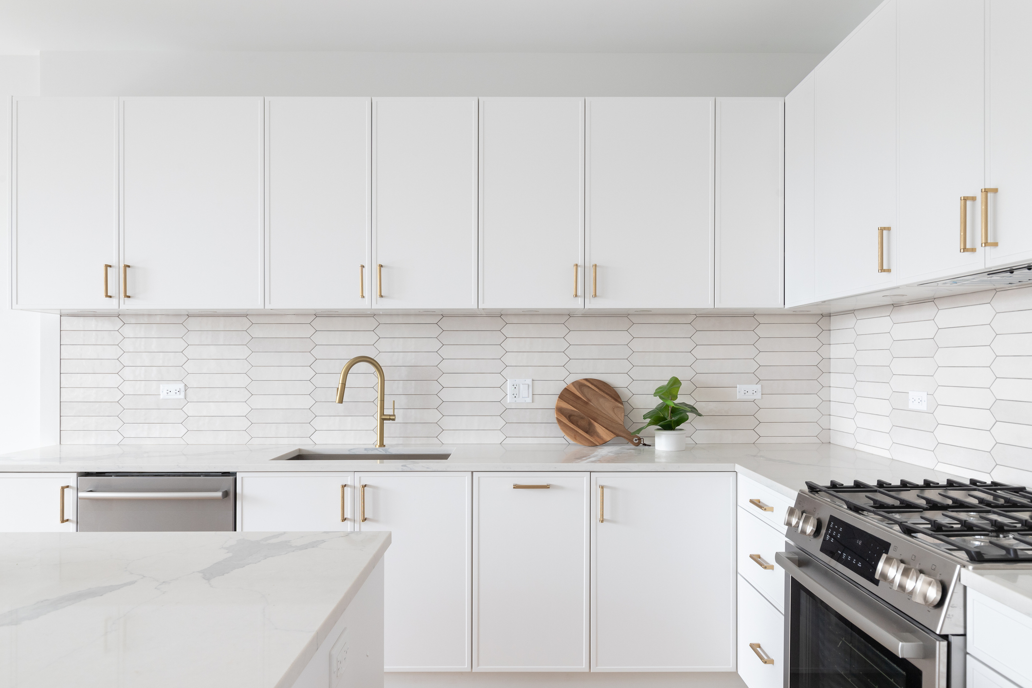 A bright white kitchen with white cabinetry, brass hardware and a marble island
